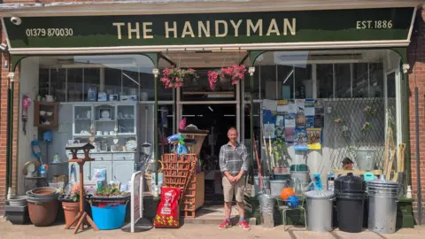 A man standing in front of a hardware shop.