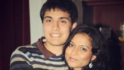 Nishat Siddiqi A black-haired boy with a stripy jumpter and brown polo neck t-shirt is smiling while embracing a smiling lady with black hair