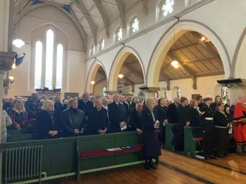 A few of the congregation standing in the pews during a church service.