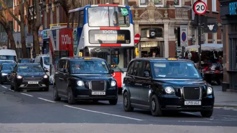 Getty Images Two black cabs and a London bus drive down a London street 