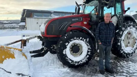 Tractor driver Duncan Wight standing next to his snow-covered tractor.