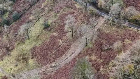 Westmorland and Furness Council An aerial view of the hillside below the road. A large dirt track has been created by the landslip. It runs from the road all the way down the hill.