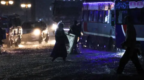 EPA/Shutterstock Kenyans cross flooded roads during heavy rain in Nairobi, Kenya