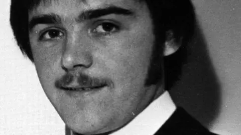 A black and white image showing Brendan Megraw. He was a 22-year-old man who is pictured with dark hair and a moustache, wearing a white shirt.