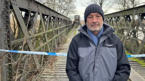 Roddy Robertson standing at the Spey Viaduct, the damaged section is visible in the distance, and there is police tape behind him.