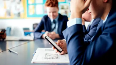 Getty Images Schoolboy holding a mobile phone in classroom