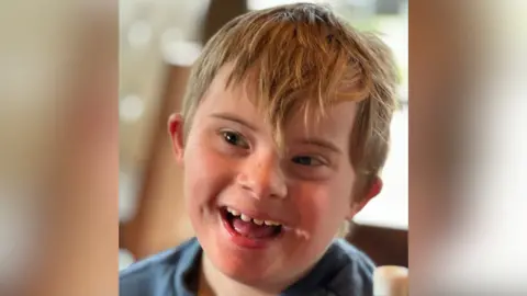 A young child with dark blonde hair smiling.