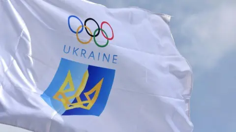 White flag of the National Olympic Committee of Ukraine, featuring the Olympic rings above the word Ukraine and a blue and yellow crest