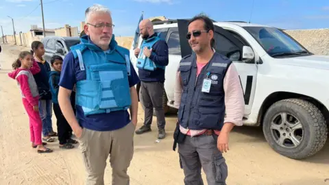 FDCO / UK-Med Picture of David Anderson in a blue flack jacket in Gaza he is standing with a fellow medic in front of a white UN 4x4.