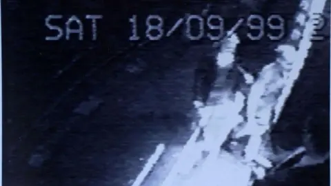 PA Media Grainy black-and-white CCTV image shows two young women walking from the road into a nightclub. A doorman, dressed in suit and tie, looks at them as they enter. A digital caption across the top of the image reads: "SAT 18/09/99".