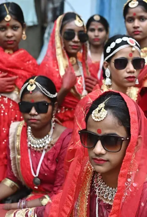 Model Inovasi untuk Perubahan Anak-anak di peragaan busana yang menjadi viral di India, foto close-up tujuh gadis dalam satu kelompok, semuanya mengenakan pakaian merah warna-warni, perhiasan Maang Tikka, dan kacamata hitam.