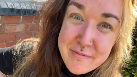 A woman with long brown hair and piercings in her nose and lips