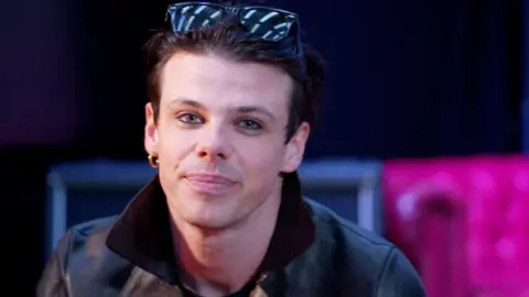 A head and shoulders image of Yungblud, who is wearing a leather jacket and sunglasses on his head while looking into the camera