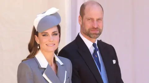 PA Media The Princess of Wales wearing a grey coat dress with white detail on the lapels and a grey and white hat - the Prince of Wales has a dark suit with pale blue waistcoat and a dark blue tie 