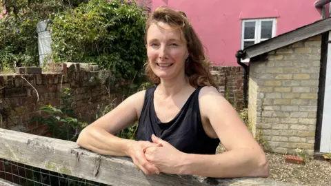 Shaun Whitmore/BBC Alex Stevenson smiling at the camera while standing in her farm and wearing a black tank top 