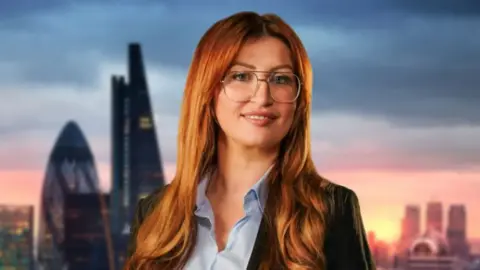 Michaela has red hair and wears glasses. She wears a shirt and blazer and stands in front of a London backdrop in a promotional picture.