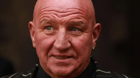 PA Media An image from 2013 showing Dave Courtney dressed in a black and white striped suit with a black shirt and wearing an earring in his left ear