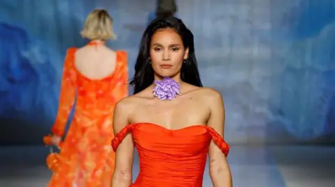 Getty Images Uma modelo desfila no desfile de moda de Shein vestindo uma camisa laranja