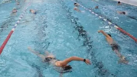 The inside of a swimming pool with the water divided into lanes with people swimming