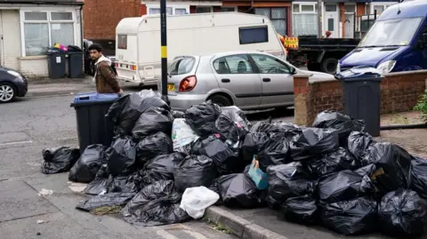 PA Bin bags piled up on a pavement at the junction of a residential street.