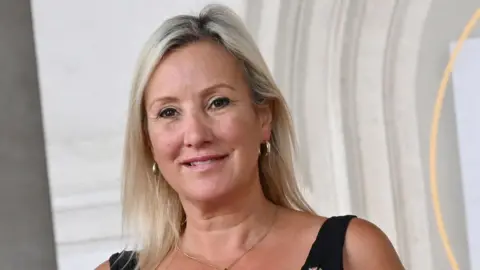Getty Images Gosport MP Caoline Dinenage smiles in the direction of the camera. She has long blonde hair and gold hooped earrings. She is wearing a black top with shoulder straps. 