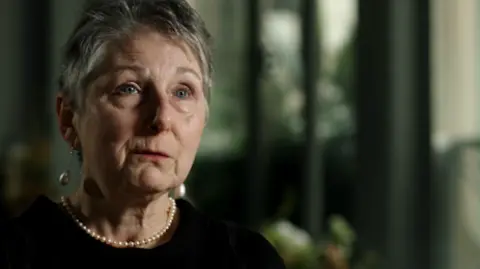 Rosemary Agnew, a woman with short grey hear, wearing a black top and pearl earrings and necklace.