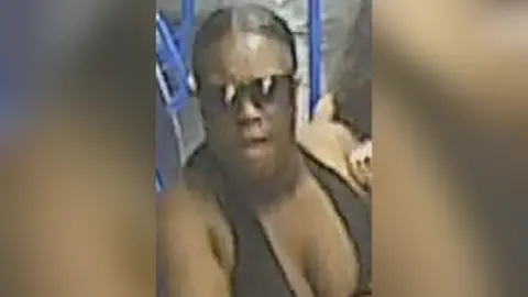 CCTV photo shows a black woman with dark hair, sunglasses and black top.  