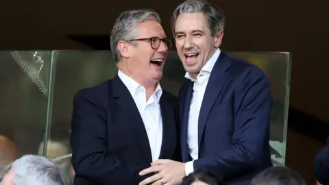 REUTERS/Damien Eagers Sir Keir Starmer and Simon Harris clasping hands and laughing in the Aviva stadium stands before the Republic of Ireland v England football match