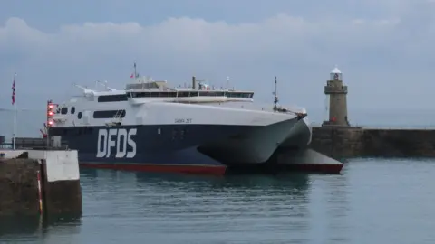 BBC A blue ferry with the letters DFDS written on the side. The boat is a catamaran and has the name Tarifa Jet on it. 