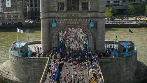 Getty Images An aerial view of a sea of marathon participants running across Tower Bridge, with the River Thames visible on either side.