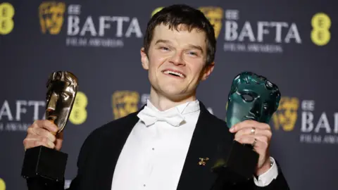 EPA Robert Aramayo holding up two Bafta trophies