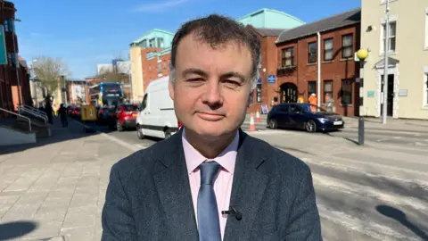 Councillor Gary Ridley stands in front of a zebra crossing.
