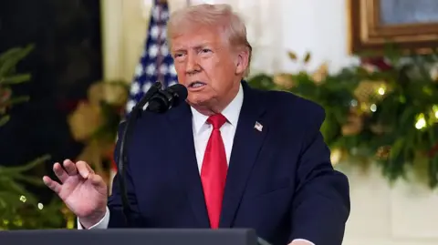 Trump, wearing a blue suit and red tie, speaks into a microphone will delivering an address to the nation from the White House.
