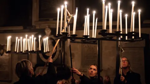 Getty Images A close up of three people lighting dozens of candles in darkness in Salisbury Cathedral