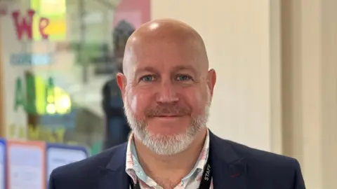 George King/BBC A head shot of Phil Stittle. He has white facial hair and is wearing a blazer over a shirt. He is smiling into the camera.