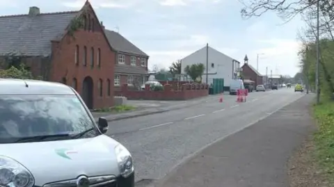 White small van with green stripe on road at Bagillt in Flintshire. The road closed and police vehicle in the distance beyond a closed sign