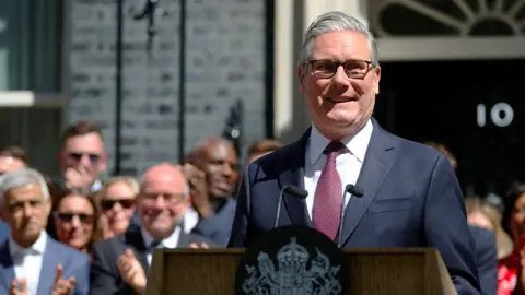 Keir Starmer smiling after giving final speech as Prime Minister on Downing street wiyth clapping crowd behind him