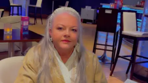 Caroline Heaven Silver-haired Caroline Heaven, wearing a yellow jacket and white top, relaxes in a chair