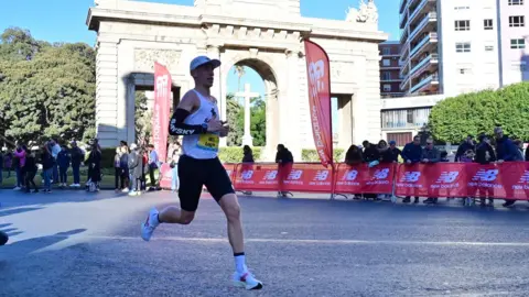 UGC Logan Smith is seen running the Frankfurt Marathon. There are red barriers behind the runner with branded.