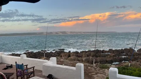 Curtis Miller Fishing rods set up on socks by the sea in Mossel Bay, South Africawith blue sky and pink clouds.