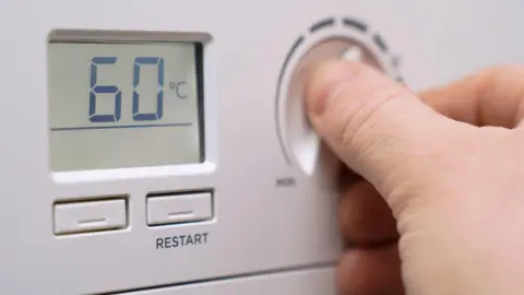 PA A hand turning the dial on a thermostat which shows the temperature as 60 degrees Celsius.