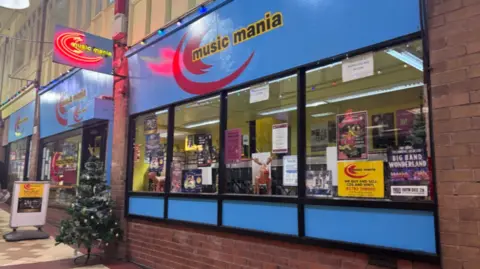 A shop frontage with Music Mania in large letters across the top. There is a Christmas tree outside