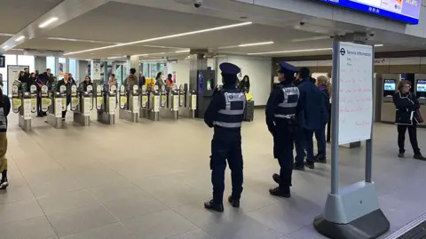 A line of officers are standing infront of the ticket barriers