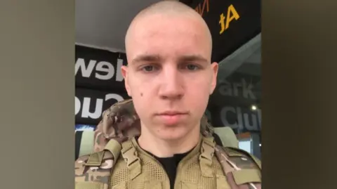 Olesia Khrapova Maksym Khrapov is dressed in a military uniform and looks straight into the camera. He has a shaved head.