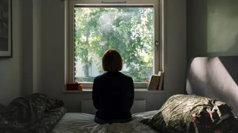 Silhouette of a woman sitting on a bed looking out a window