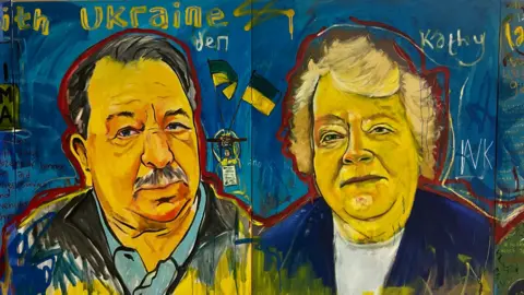 Side-by-side paintings depicting an older man and woman. They are painted on a blue background. The man has dark grey hair combed over to one side, a similarly coloured moustache, and is wearing a blue shirt and a dark jacket. The woman has short blonde hair and is wearing a whit top and a blue jacket.