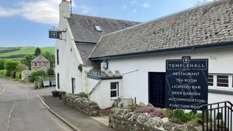 A white pub building in the Borders with a sign for the Templehall Hotel in front of it