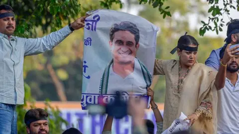 Getty Images A few men and a woman - as part of a Youth Congress stage a demonstration in Delhi on 24 February. They hold a poster of the group's national president Uday Bhanu Chib, who has been arrested by the police.