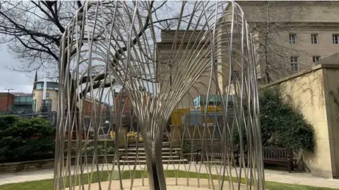 A steel memorial shaped like a willow tree, Sheffield City Hall is in the background