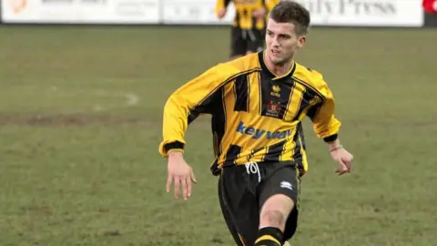 Richard Richard wearing a yellow and black top and black shorts playing in a football match.